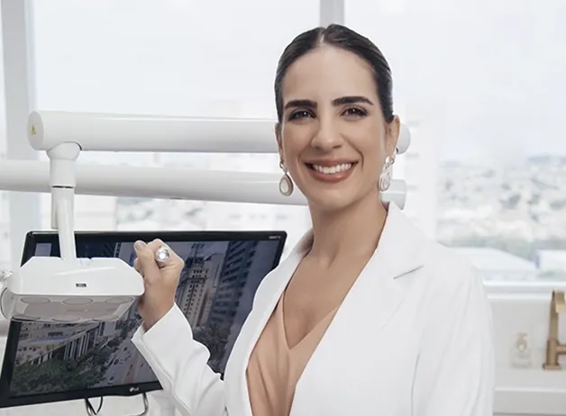 Dra. Caroline Bianchi ao lado do monitor e do equipamento de atendimento